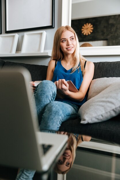 Pensativo hermosa mujer joven sentada y leyendo el libro en casa