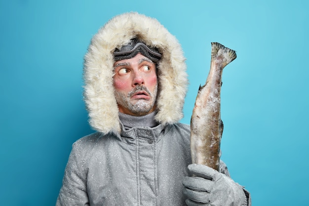 pensativo hombre sin afeitar congelado sostiene grandes peces trofeo capturados en el lago helado tiene descanso activo durante el invierno usa chaqueta.