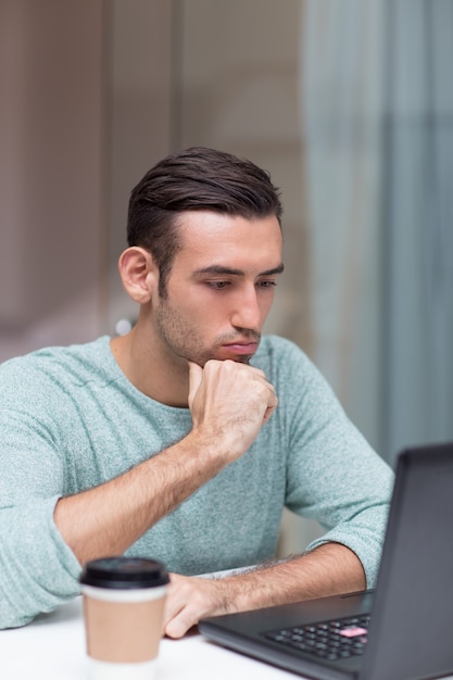 Pensativo hombre guapo trabajando en la computadora portátil en casa