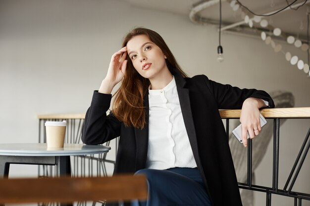 Pensativo joven empresaria sentado cafe, mirando lejos soñadora