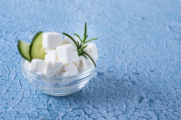 Pepino de queso feta y hierbas en un recipiente sobre fondo azul.