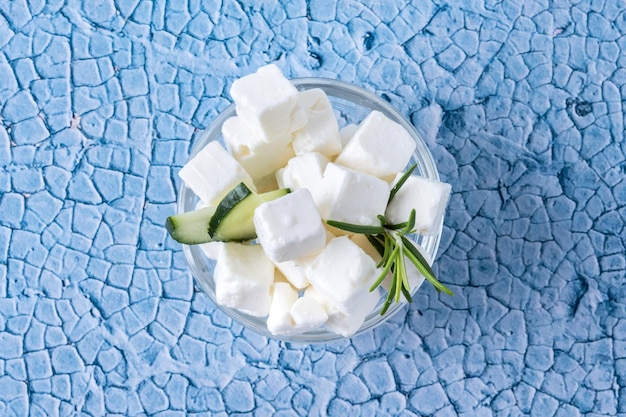 Pepino de queso feta y hierbas en un recipiente sobre fondo azul.