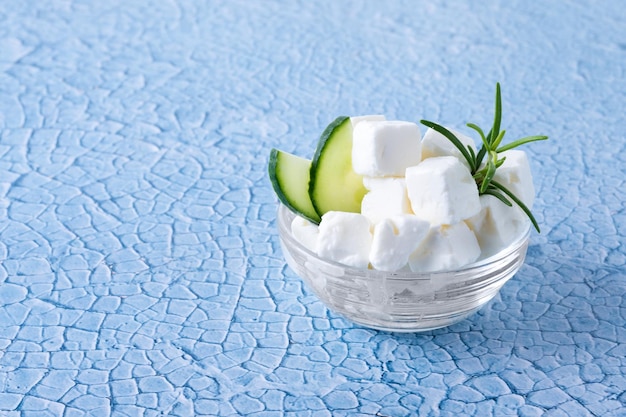 Pepino de queso feta y hierbas en un recipiente sobre fondo azul.