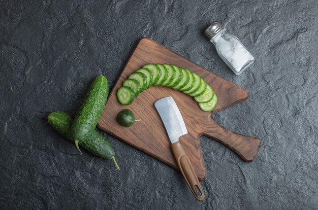 Pepino en rodajas o entero sobre tabla de madera con sal y cuchillo. Foto de alta calidad