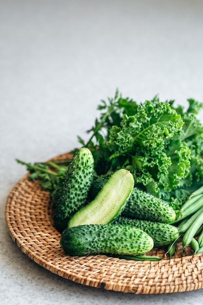 pepinos, col y frijoles verdes en un plato de mimbre en la mesa de la cocina