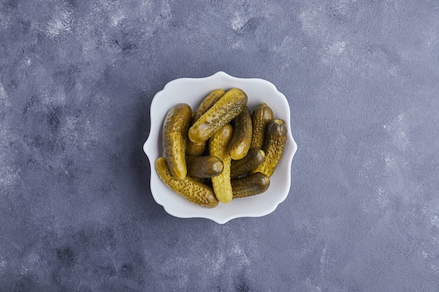 Pepinos encurtidos en plato blanco sobre fondo azul.