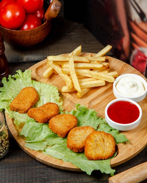 Foto gratuita pepitas fritas con papas fritas sobre tabla de madera