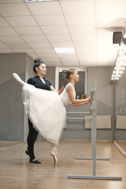 Pequeña bailarina linda en traje de ballet blanco. La señorita está bailando en la habitación. Chica en clase de baile con profesora.