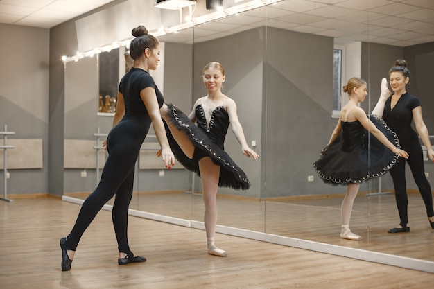 Pequeña bailarina linda en traje de ballet negro. La señorita está bailando en la habitación. Chica en clase de baile con profesora.