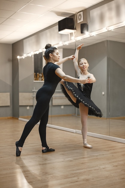 Pequeña bailarina linda en traje de ballet negro. La señorita está bailando en la habitación. Chica en clase de baile con profesora.