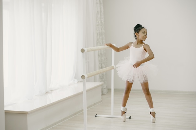 Pequeña bailarina linda en traje de ballet rosa. Niño en zapatos de punta está bailando en la habitación. Niño en clase de baile.