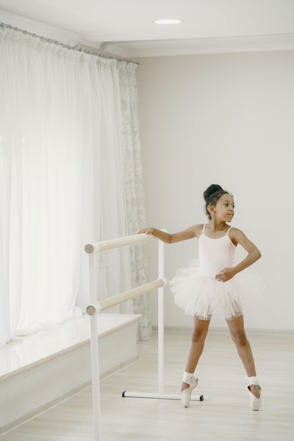 Pequeña bailarina linda en traje de ballet rosa. Niño en zapatos de punta está bailando en la habitación. Niño en clase de baile.