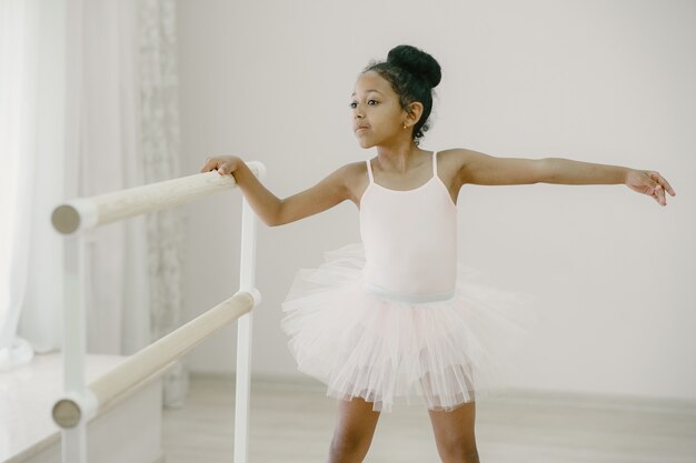 Pequeña bailarina linda en traje de ballet rosa. Niño en zapatos de punta está bailando en la habitación. Niño en clase de baile.