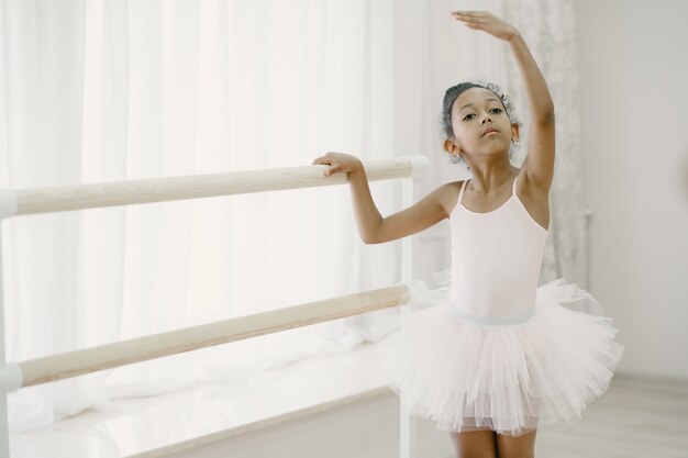 Pequeña bailarina linda en traje de ballet rosa. Niño en zapatos de punta está bailando en la habitación. Niño en clase de baile.