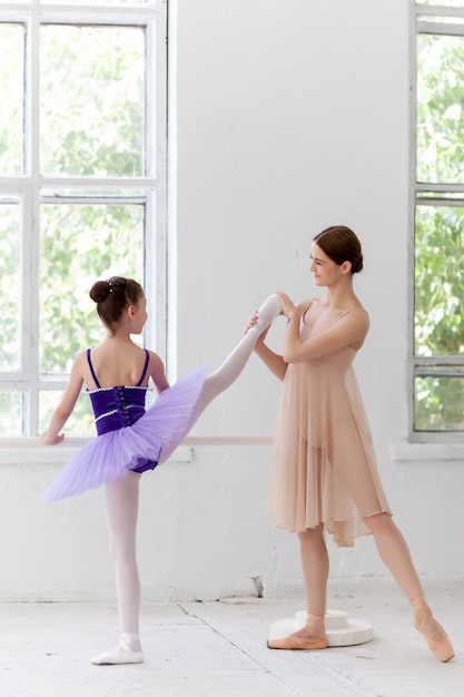 Pequeña bailarina posando en la barra de ballet con maestra personal en estudio de danza