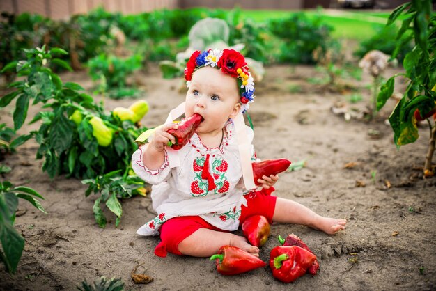 La pequeña bebé con un pimiento rojo grande se sienta en el patio trasero