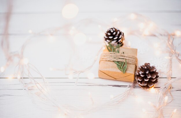 Pequeña caja de regalo en una envoltura cerca de enganches y luces de hadas iluminadas