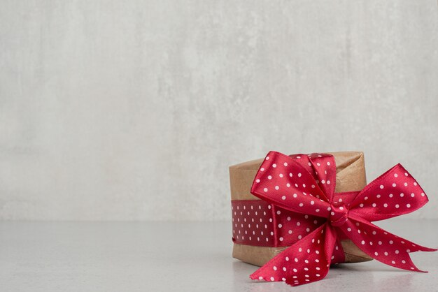 Una pequeña caja de regalo con lazo rojo en la pared blanca.