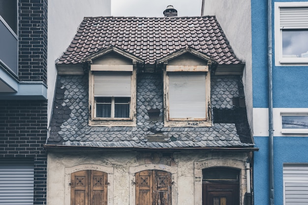 Pequeña casa envejecida y antigua entre dos casas nuevas y modernas