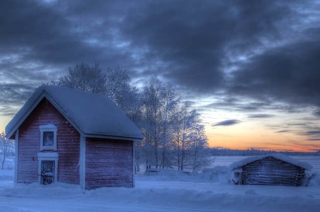Pequeña casa de madera en el campo cubierto de nieve durante la puesta de sol