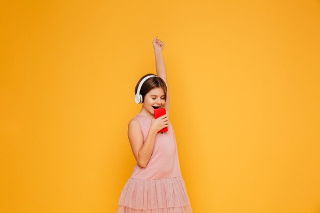 Pequeña dama en auriculares cantando en smartphone aislado