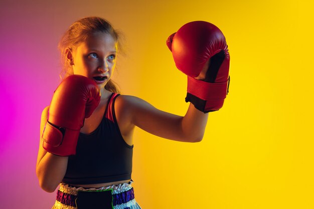 Pequeña formación caucásica de kick boxer femenino sobre fondo degradado en luz de neón, activa y expresiva