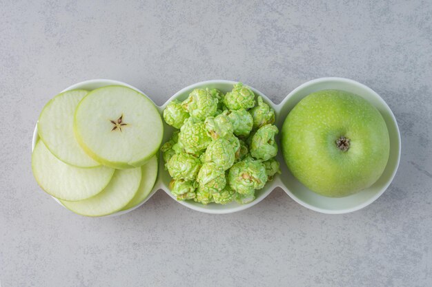 Una pequeña fuente de manzanas y palomitas de maíz en la superficie de mármol.