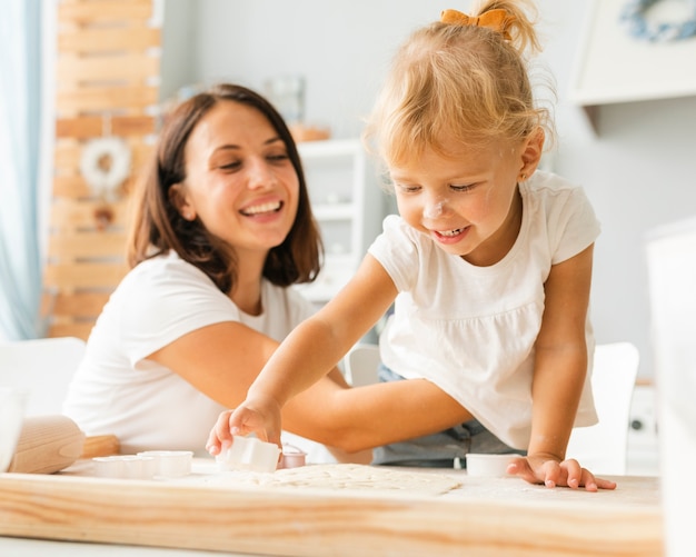 Pequeña hija cortando masa para galletas