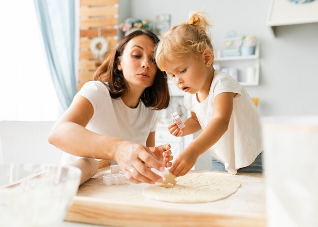 Pequeña hija curiosa y madre preparando galletas
