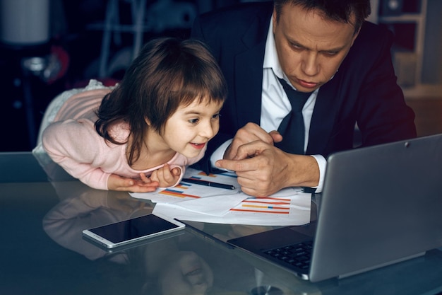 Pequeña hija y hombre de negocios mirando atentamente videos en una laptop. padre teniendo un descanso del trabajo.