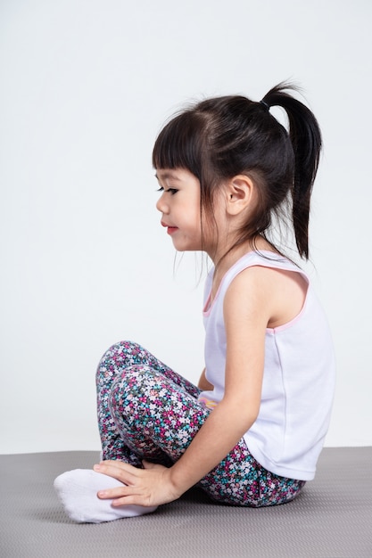 Pequeña hija sentada en la almohadilla de yoga para hacer ejercicio