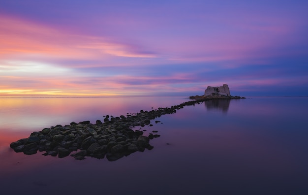 Una pequeña isla en medio del océano bajo un cielo pintado con múltiples colores.