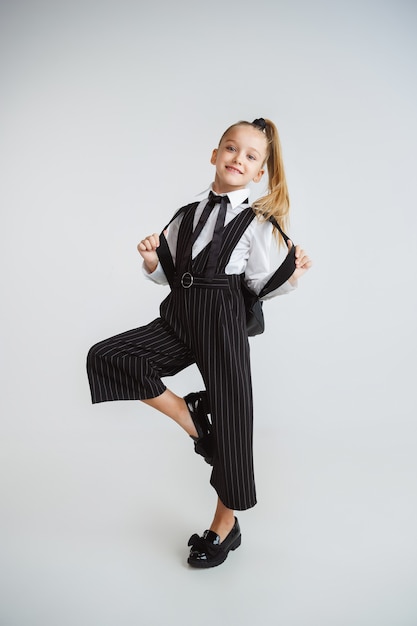 Pequeña modelo femenina posando en uniforme escolar en la pared blanca del estudio