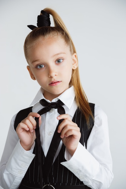 Pequeña mujer caucásica modelo posando en uniforme escolar sobre fondo blanco.