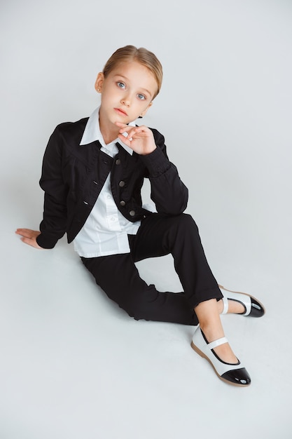 Pequeña mujer caucásica modelo posando en uniforme escolar sobre fondo blanco.