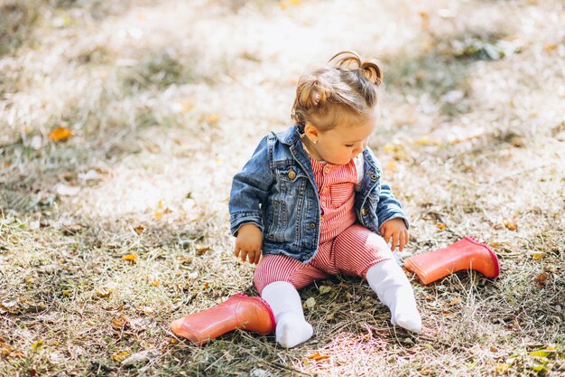 Pequeña niña con botas de lluvia sentado en el parque