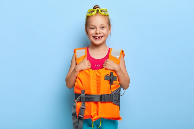 Pequeña niña hermosa lista para viaje en barco, usa gafas y chaleco salvavidas