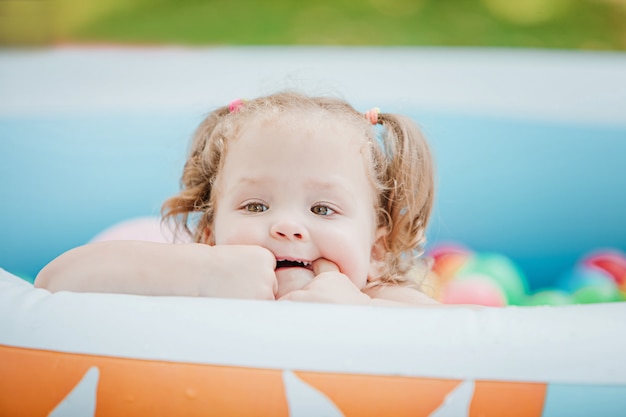 La pequeña niña jugando con juguetes en la piscina inflable en el día soleado de verano