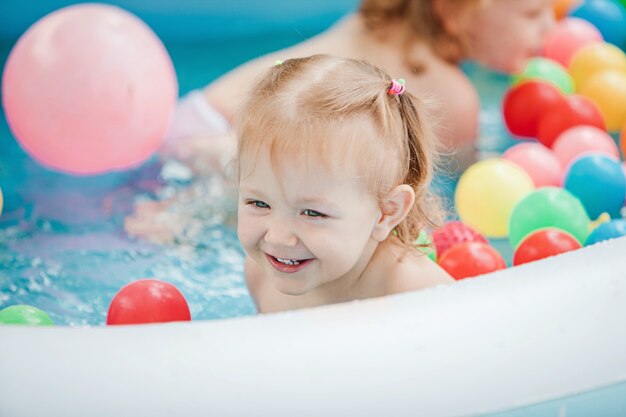 La pequeña niña jugando con juguetes en la piscina inflable en el día soleado de verano