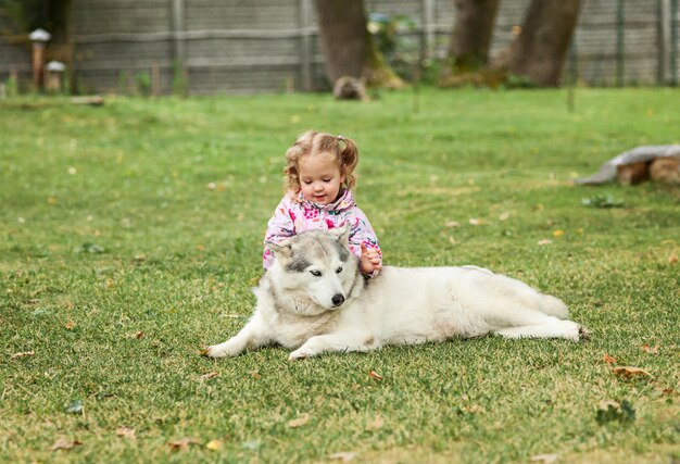 La pequeña niña jugando con perro contra la hierba verde en el parque