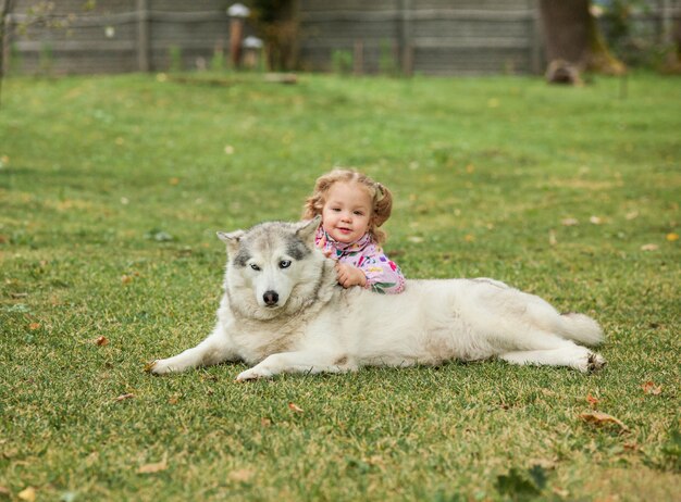 La pequeña niña jugando con perro contra la hierba verde en el parque