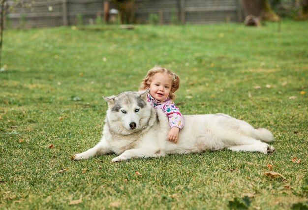La pequeña niña jugando con perro contra la hierba verde
