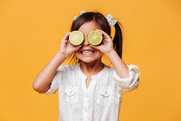 Pequeña niña linda que cubre ojos con la cal.