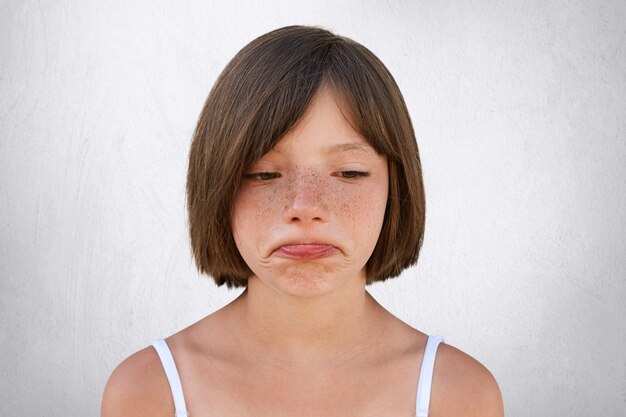 La pequeña niña molesta con piel pecosa y cabello ondulado, curvando sus labios con expresión de horror, infeliz al descubrir que los padres no compraron su juguete. Pecosa hermosa chica va a llorar