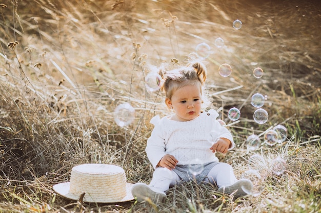 Pequeña niña soplando pompas de jabón en el campo