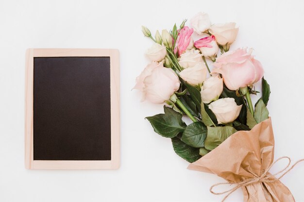 Pequeña pizarra de madera en blanco con ramo de flores sobre fondo blanco