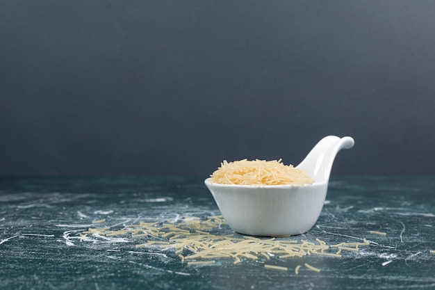 Una pequeña placa blanca con fideos sin preparar sobre fondo de mármol