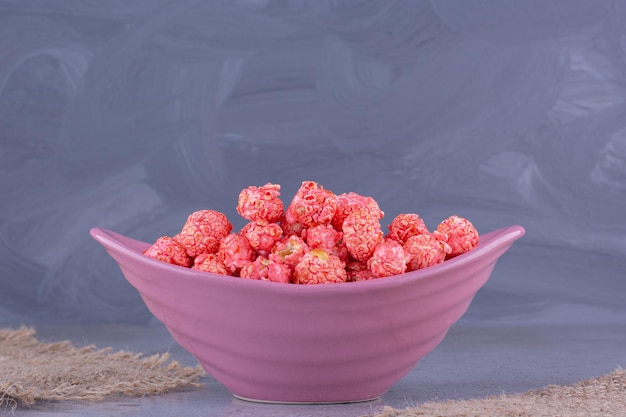 Una pequeña porción de dulces de palomitas de maíz de color rojo apilados en un recipiente junto a trozos de tela sobre fondo de mármol. Foto de alta calidad