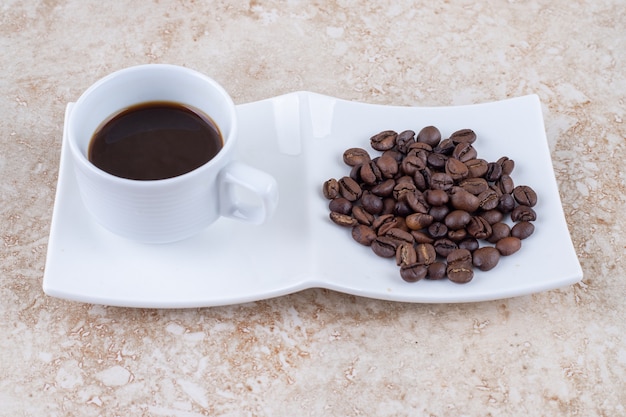 Una pequeña taza de café junto a un montón de granos de café.