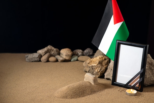 Pequeña tumba con bandera palestina y piedras en el escritorio oscuro muerte de la guerra de Palestina